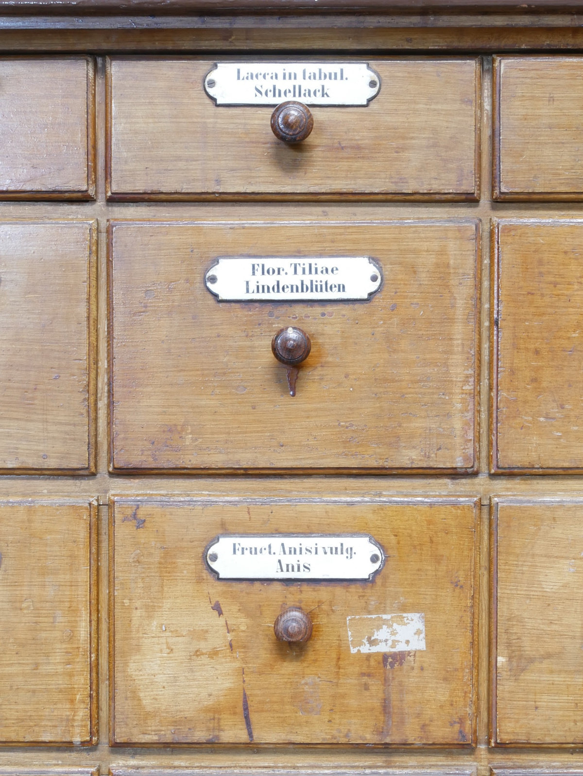Detailaufnahme einzelner Schubladenfronten mit originalen Griffen, Etikettenhaltern und gewachsener Holzoberfläche der historischen Apothekeneinrichtung.