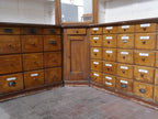 Eckansicht der historischen Apothekeneinrichtung mit zahlreichen originalen Schubladen und massiven Unterschränken. Die Aufnahme verdeutlicht die großzügige Bauweise der gesamten Ladeneinrichtung.