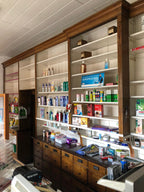 Historische Apothekeneinrichtung im aufgebauten Zustand mit eingeräumten Regalen. Die Aufnahme zeigt die originale Nutzung als Verkaufs- und Präsentationseinrichtung in einer Apotheke oder Drogerie.