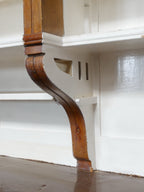 Detailaufnahme einer geschwungenen Jugendstil-Konsole unter den offenen Regalböden. Die elegante Formgebung und die originale Holzbearbeitung unterstreichen den historischen Charakter der Apothekeneinrichtung.