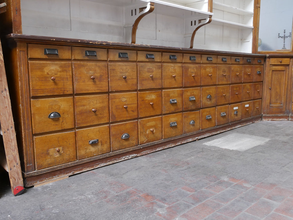 Lange Frontansicht der originalen Schubladenschränke mit zahlreichen leichtgängigen Schubladen und originalen Metallgriffen aus einer historischen Apotheke oder Drogerie.