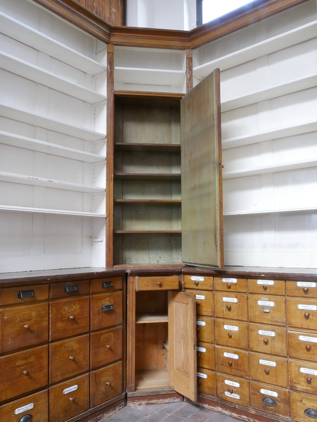 Seitenansicht der offenen Regale mit darunterliegenden originalen Schubladenschränken. Die Kombination aus Stauraum und Präsentationsfläche ist typisch für historische Apothekenmöbel.