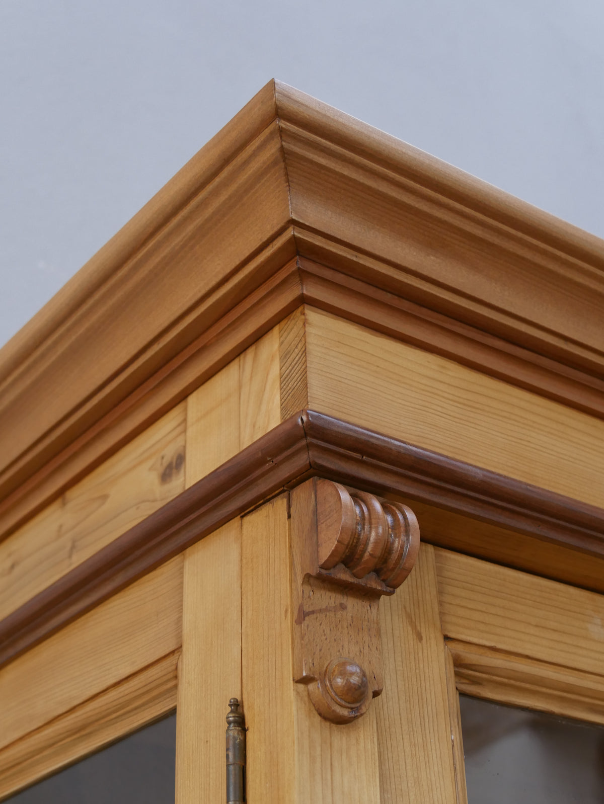Nahaufnahme der profilierten Kranzleiste der restaurierten Bibliotheksvitrine. Die aufwendig gearbeitete Holzverzierung und die gewachste Oberfläche betonen die hochwertige handwerkliche Verarbeitung.