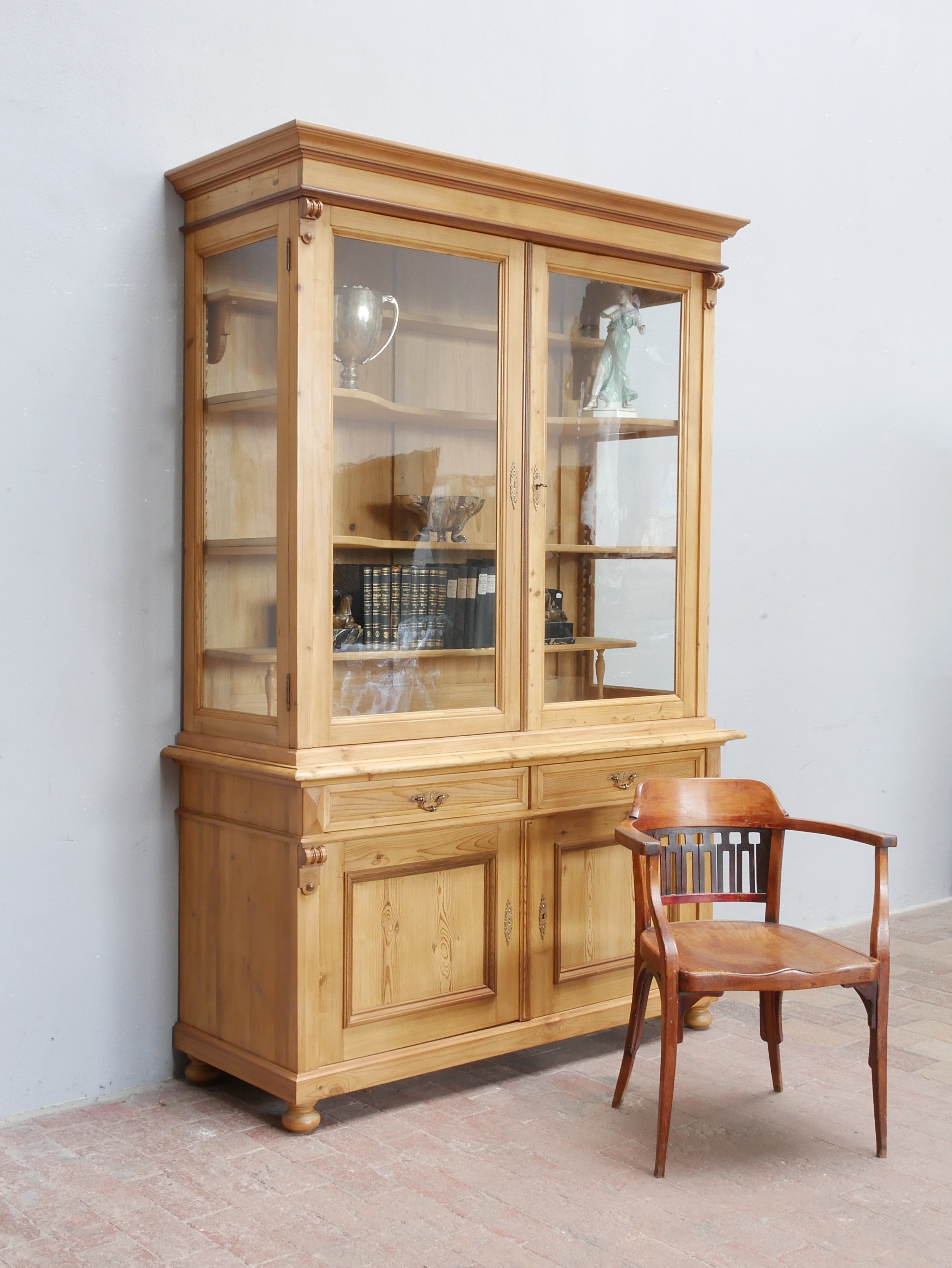 Seltene antike Bibliotheksvitrine aus Weichholz von etwa 1890 in restauriertem Zustand. Die große zweiteilige Vitrine mit dreiseitig verglastem Oberteil, originalen Glasscheiben, dekorativer Kranzleiste und geschlossenem Unterbau zeigt die vollständige Frontansicht des historischen Laden- und Bücherschranks.