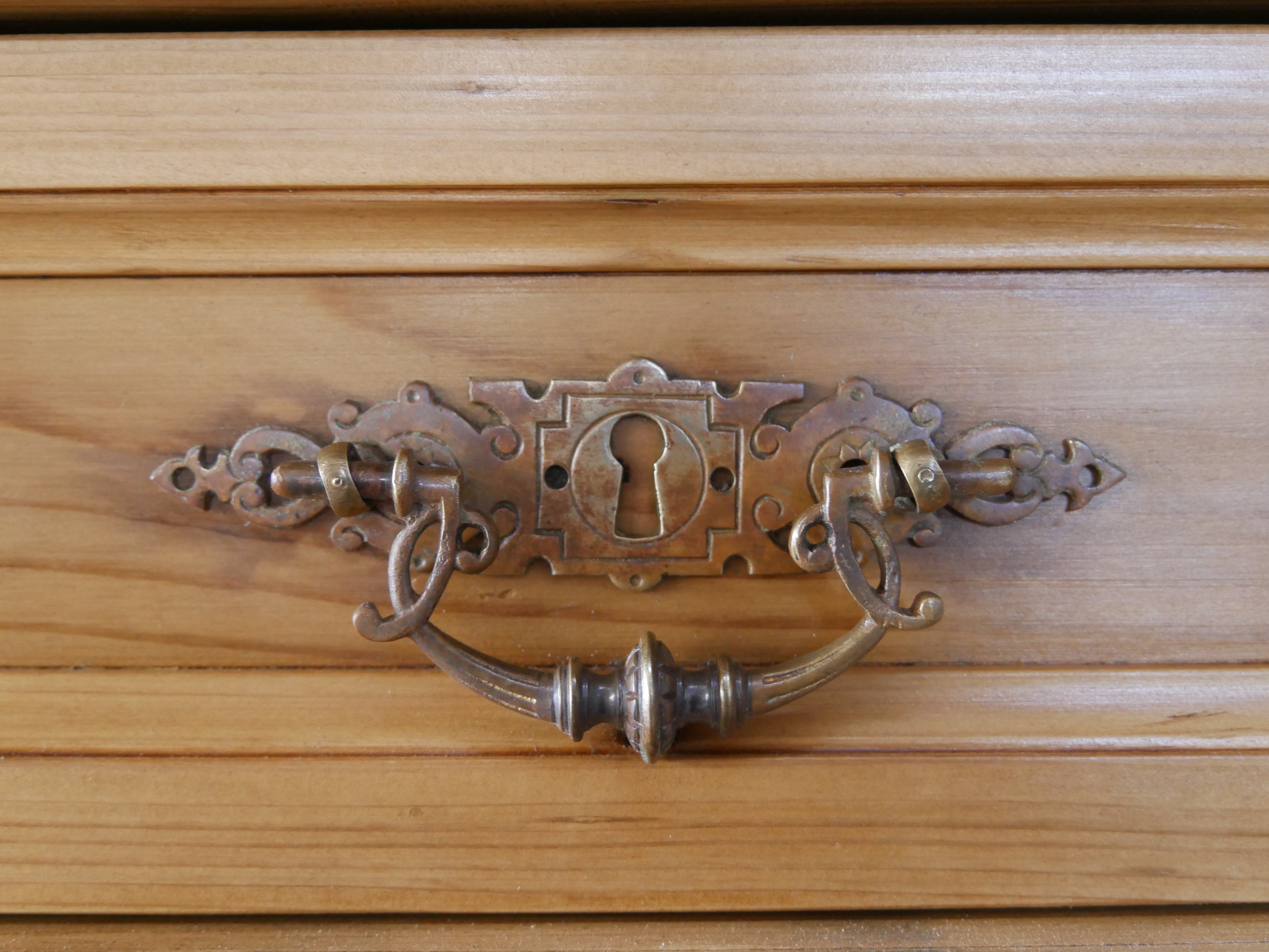 Detailaufnahme eines originalen historischen Möbelbeschlags mit kunstvoll gearbeitetem Griff. Die fein gearbeiteten Metallbeschläge unterstreichen den authentischen Charakter der Bibliotheksvitrine von etwa 1890.