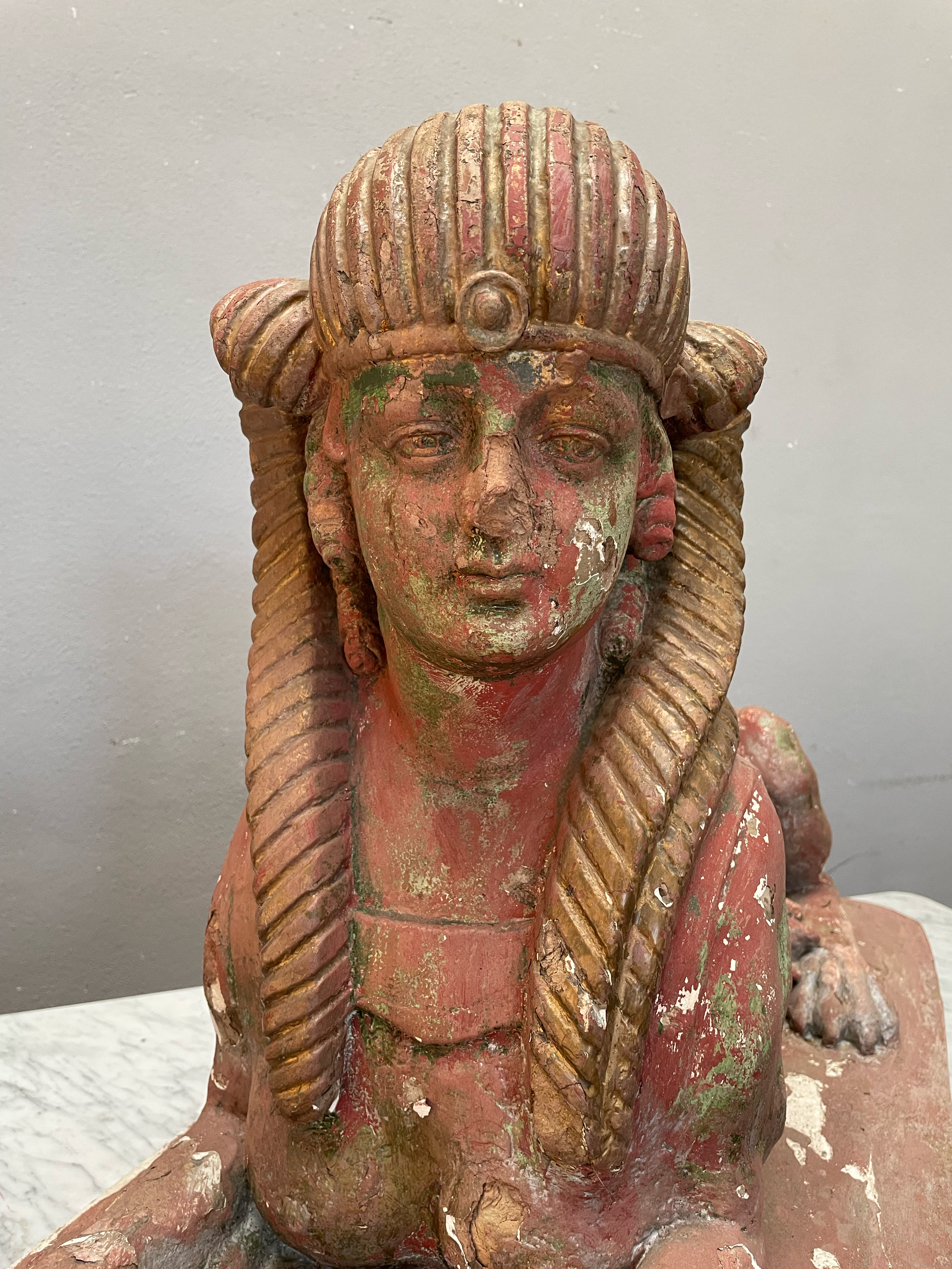 Detailaufnahme des Gesichts einer antiken Sphinx. Die fein ausgearbeiteten Gesichtszüge, das ägyptisch inspirierte Kopftuch und die authentische Patina verleihen der historischen Skulptur ihren besonderen Charakter.