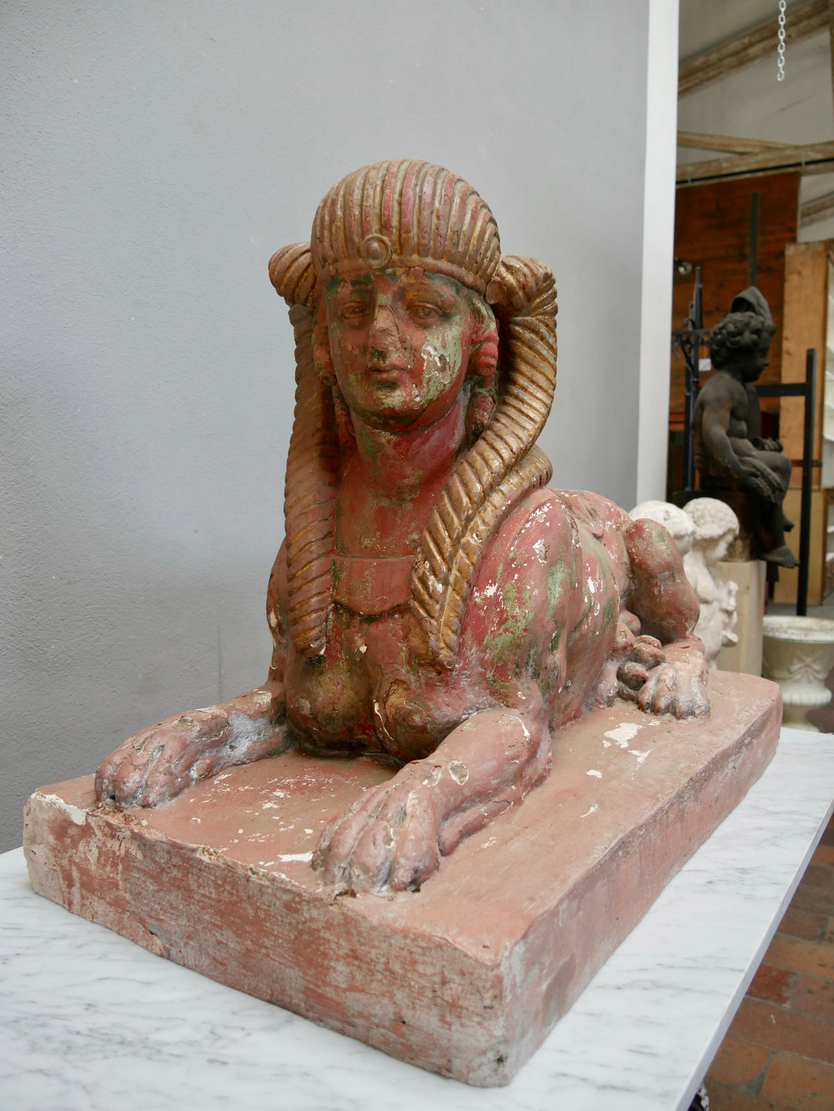 Seitenansicht einer antiken Sphinx aus Terrakotta. Die Aufnahme zeigt den liegenden Löwenkörper, den rechteckigen Sockel sowie die authentischen Alters- und Gebrauchsspuren der historischen Skulptur.