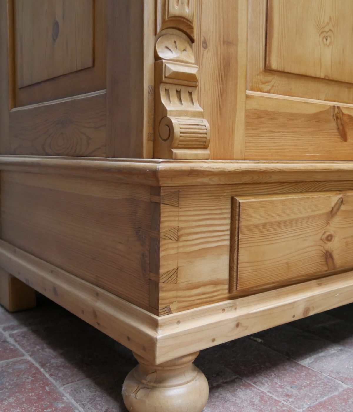 Detailaufnahme der unteren Sockelecke mit profilierter Zierleiste und Kugelfuß. Die Aufnahme zeigt die solide handwerkliche Verarbeitung und die elegante Linienführung des historischen Schranks.