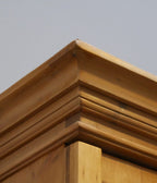 Detailansicht der aufwendig gearbeiteten Kranzleiste des restaurierten Weichholz-Lehrmittelschranks. Die feine Verarbeitung und die originale Holzstruktur sind gut erkennbar.
