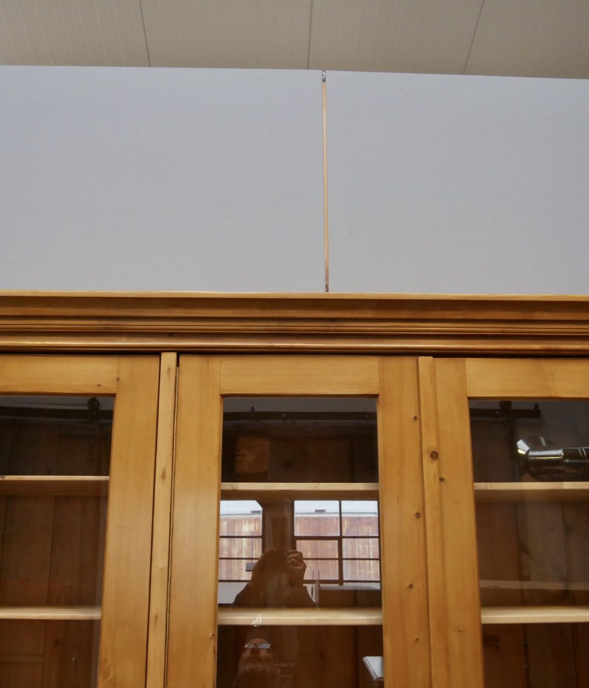 Detailaufnahme des oberen Türbereichs mit den verglasten Türen des historischen Lehrmittelschranks. Sichtbar sind die hochwertige Verarbeitung und die charakteristische Gestaltung der Vitrine.