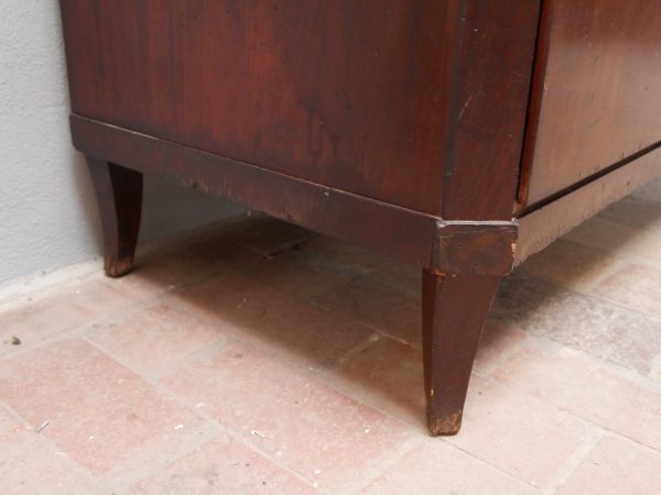 Detailansicht des Sockelbereichs mit den charakteristischen Empire-Füßen. Die massive Konstruktion und die originale Holzoberfläche unterstreichen die hohe handwerkliche Qualität der Kommode um 1810.