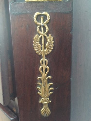 Detailaufnahme eines originalen feuervergoldeten Schlüsselschildes mit fein gearbeitetem Ornament. Der historische Beschlag unterstreicht den authentischen Charakter der Empire-Kommode.