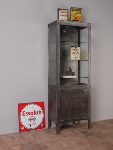 Restaurierter antiker Arzt- und Büroschrank im Industriedesign aus der Zeit um 1910–1920 in vollständiger Frontansicht. Der hohe Vitrinenschrank besitzt einen verglasten Oberteil mit drei Glas-Einlegeböden sowie einen geschlossenen Unterschrank. Die alte Farbschicht wurde fachgerecht entfernt, das Metall gebürstet und mit Spezialöl behandelt. Beide Türen sind abschließbar, die oberen Glasböden mehrfach höhenverstellbar – ein außergewöhnliches Originalmöbel für Praxis, Büro, Laden oder Wohnraum.
