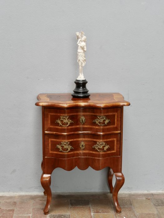 Frontansicht der kleinen Barockkommode aus Nussbaum mit geschweifter Front, zwei Schubladen, originalen Messingbeschlägen, Schlüsselloch und kunstvollen Einlegearbeiten. Die elegante Formgebung ist typisch für Dresdner Möbel um 1860.
