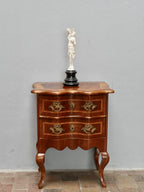 Frontansicht der kleinen Barockkommode aus Nussbaum mit geschweifter Front, zwei Schubladen, originalen Messingbeschlägen, Schlüsselloch und kunstvollen Einlegearbeiten. Die elegante Formgebung ist typisch für Dresdner Möbel um 1860.
