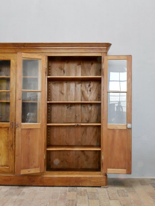 Geöffneter Bibliotheksschrank aus leicht rechter Perspektive. Die Originalverglasung, die Einlegeböden sowie der großzügige Stauraum dokumentieren den außergewöhnlich guten Originalzustand.