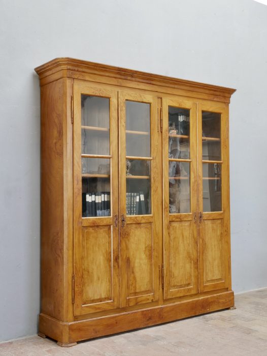 Schrägansicht von links des großen Biedermeier Bücherschranks. Die harmonischen Proportionen, die originale Bierlasur und die hochwertige handwerkliche Verarbeitung der historischen Möbelkunst kommen hervorragend zur Geltung.