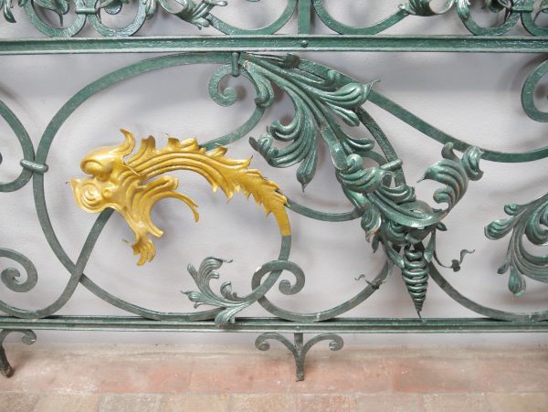 Detailaufnahme der zentralen vergoldeten Zierapplikation des historischen Schlossgeländers. Die fein modellierte Blattornamentik bildet einen eindrucksvollen Kontrast zum dunkel patinierten Schmiedeeisen und unterstreicht die exklusive Ausführung.

