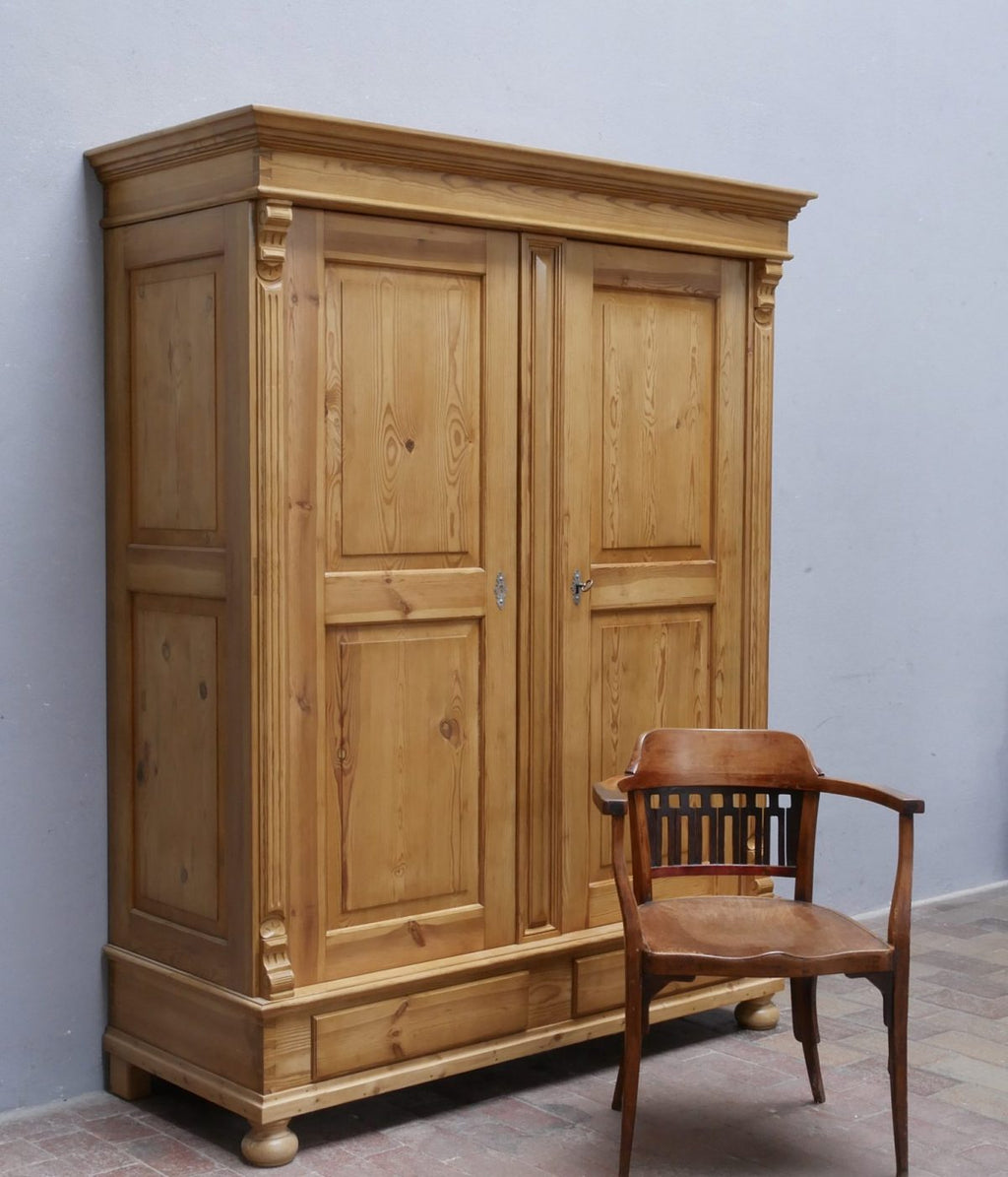 Originaler Gründerzeit Kleider- und Wäscheschrank aus Weichholz von etwa 1880 in restauriertem Zustand. Die große Frontansicht zeigt den zweitürigen Schrank mit aufwendig verzierten Füllungen, breiter Kranzleiste, massivem Sockel und eleganten Kugelfüßen.