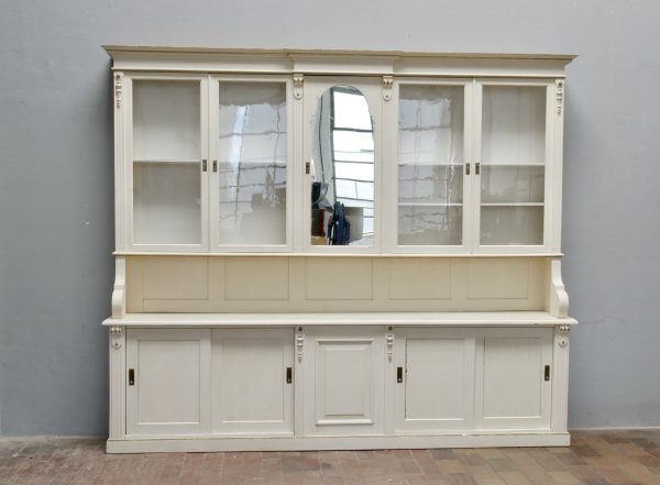 Frontalansicht des historischen Ladenschranks mit geschlossenen Schiebetüren im Oberteil. Die harmonische Gestaltung, die großzügige Präsentationsfläche und die klassische Gründerzeit-Architektur sind gut erkennbar.