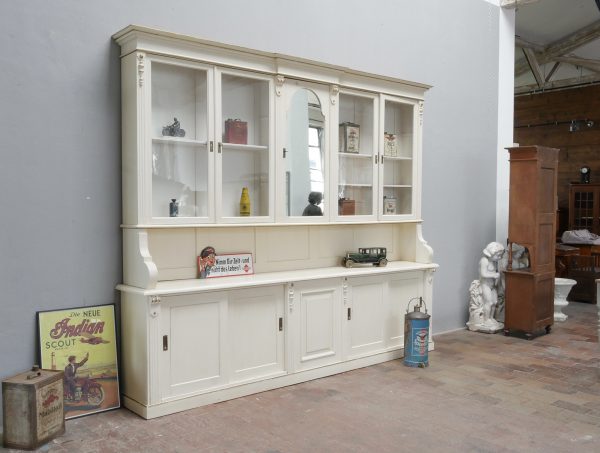 Historischer Ladenschrank mit Ladenteil aus der Gründerzeit um 1880/1890. Die Hauptansicht zeigt den zweiteiligen Schrank aus einer historischen Ladeneinrichtung mit farblich restaurierter Oberfläche in Altweiß und Cremeweiß, mundgeblasenem Originalglas, originalem Spiegelglas sowie großzügigem Unter- und Oberteil mit klassischen Gründerzeit-Verzierungen.