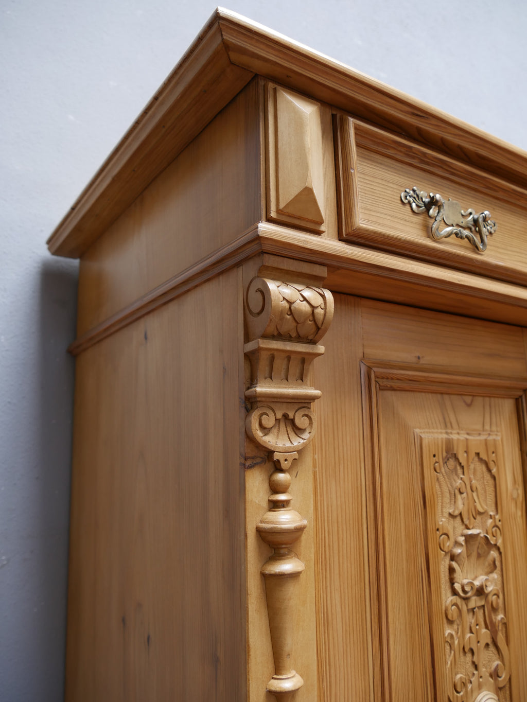Nahaufnahme eines dekorativen Originalbeschlags am restaurierten Gründerzeit-Vertiko. Der kunstvoll gestaltete Metallbeschlag hebt sich deutlich von der warmen Weichholzoberfläche ab. Die detailreiche Formgebung unterstreicht den historischen Charakter und die aufwendige Ausstattung des Vertikos aus der Zeit um 1870.