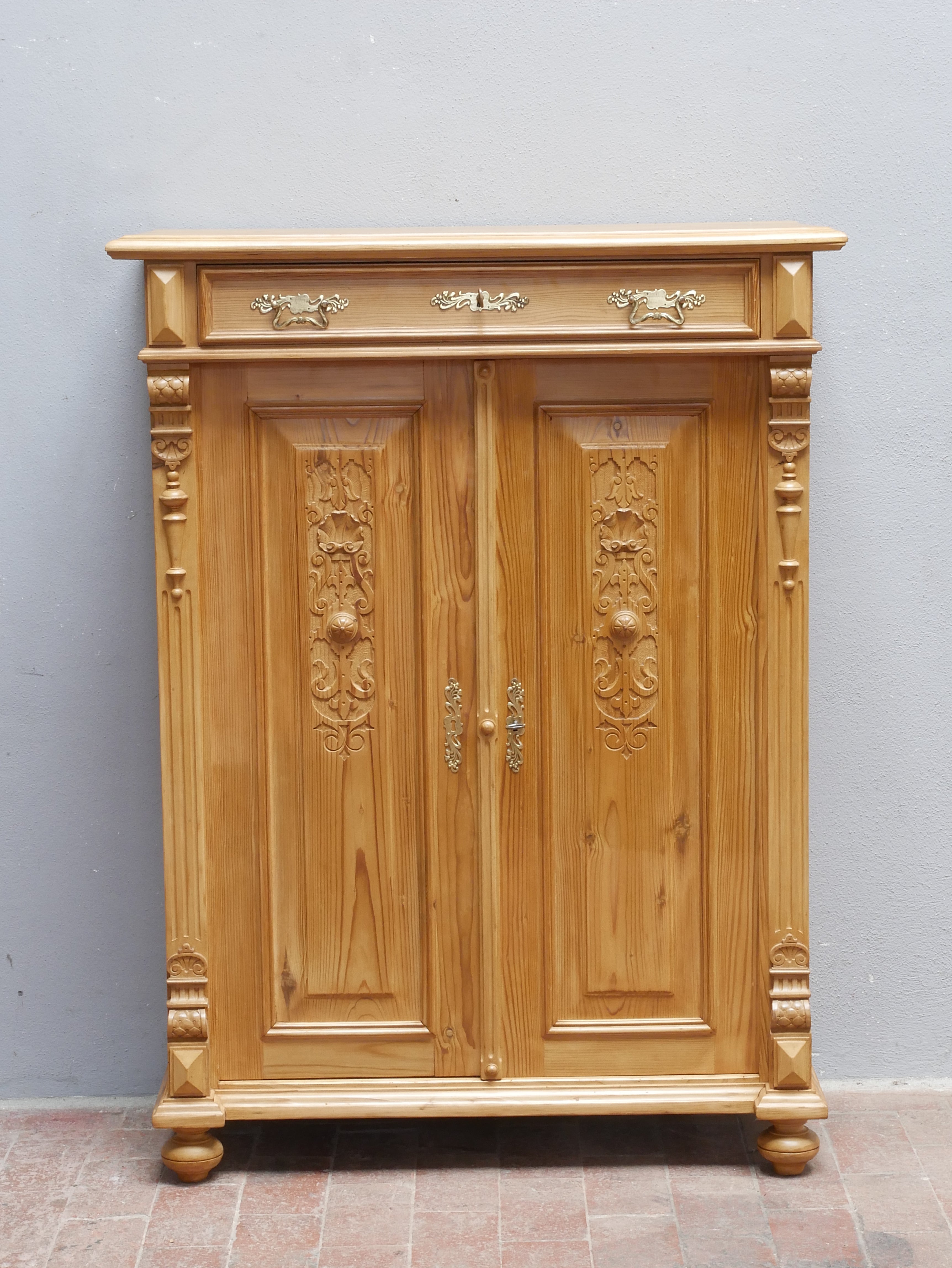 Frontale Detailansicht des restaurierten Gründerzeit-Vertikos aus Weichholz, um 1870. Beide Türen sind geschlossen und zeigen die geschnitzten, zeittypischen Gründerzeit-Ornamente. Zu sehen sind außerdem der profilierte obere Abschluss, dekorative seitliche Elemente, die originalen Beschläge und die charakteristische Sockelgestaltung des historischen Möbels.