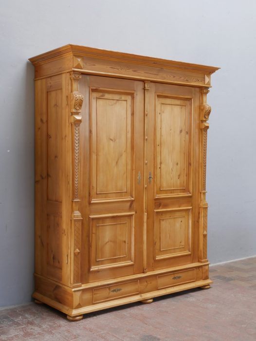 Schrägansicht des originalen Gründerzeit-Hallenschranks aus leicht linker Perspektive. Die Aufnahme zeigt die aufwendig gestaltete Seitenansicht mit zwei Seitenfüllungen sowie die reich profilierte Kranzleiste und den massiven Sockelbereich.