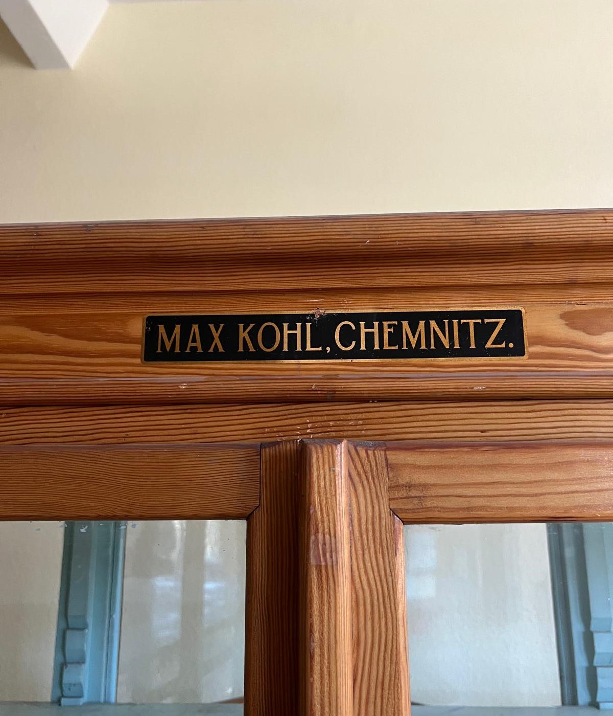Detailaufnahme des originalen Herstellerschildes „Max Kohl Chemnitz“ am oberen Bereich des historischen Lehrmittelschranks. Das Schild dokumentiert die authentische Herkunft des Museumsmöbels.