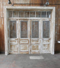 Große originale historische Türanlage aus Frankreich, datiert um 1900 im Jugendstil. Die vierflügelige Eingangsanlage mit passender Türzarge und mehrteiligem Oberlichtfenster besitzt satinierte Glasscheiben mit dekorativen Jugendstilmotiven und zeigt die komplette Frontansicht der beeindruckenden Türanlage.