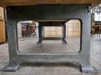 Blick unter den Tisch auf das massive Untergestell aus Gusseisen. Die schweren Maschinenfüße mit originaler grüner Lackierung und historischer Patina zeigen die stabile Konstruktion des originalen Tisches aus der Zeit um 1915–1920.