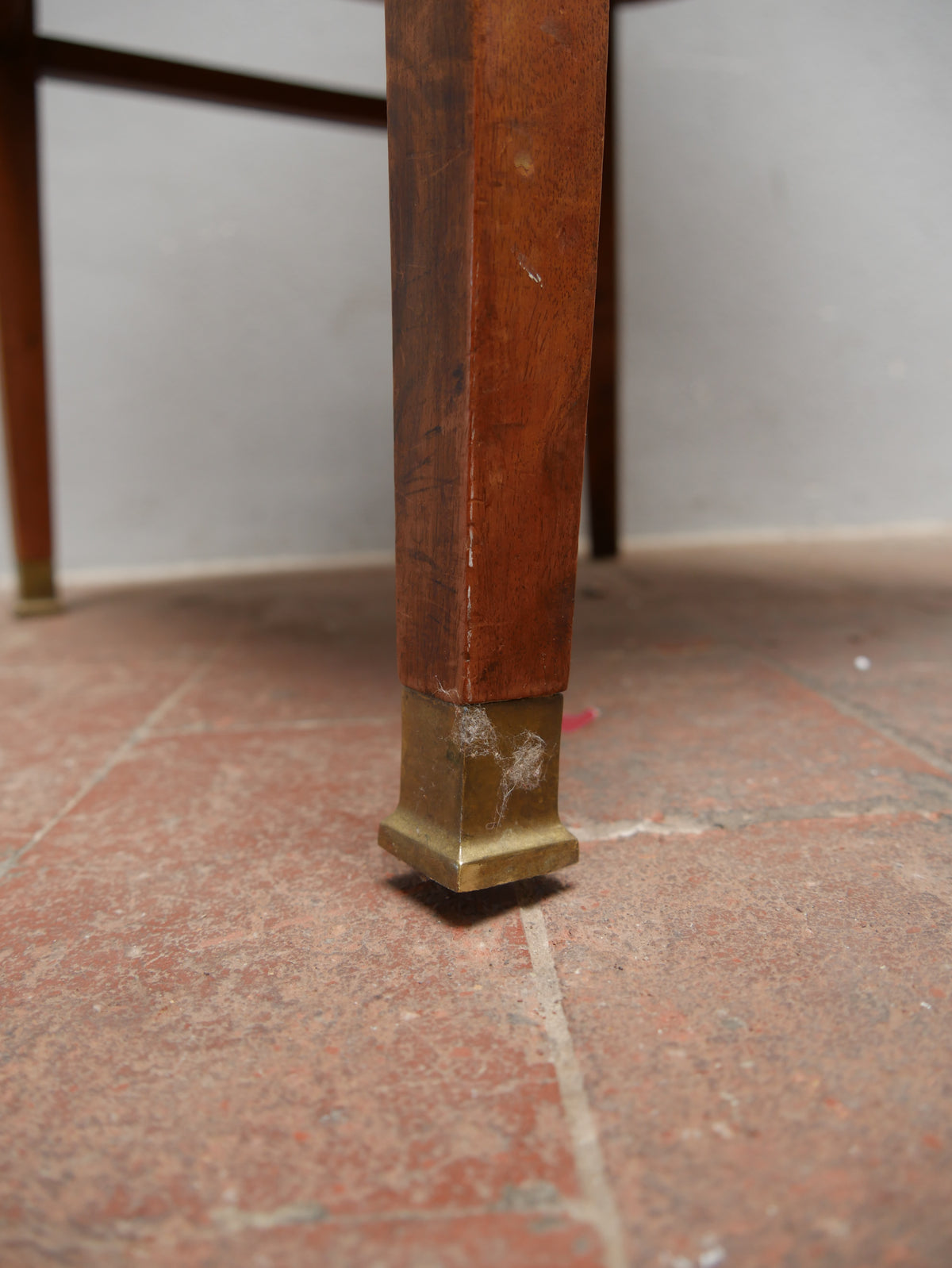 Detailaufnahme eines vorderen Stuhlbeins mit originalem Messingfüßchen am Jugendstil-Armlehnstuhl. Das Bild zeigt den Übergang vom schlanken Nussbaumholzbein zum dekorativen Messingfuß. Das historische Detail ist typisch für die hochwertige Ausführung des um 1905 entstandenen Wiener Jugendstil-Sitzmöbels.