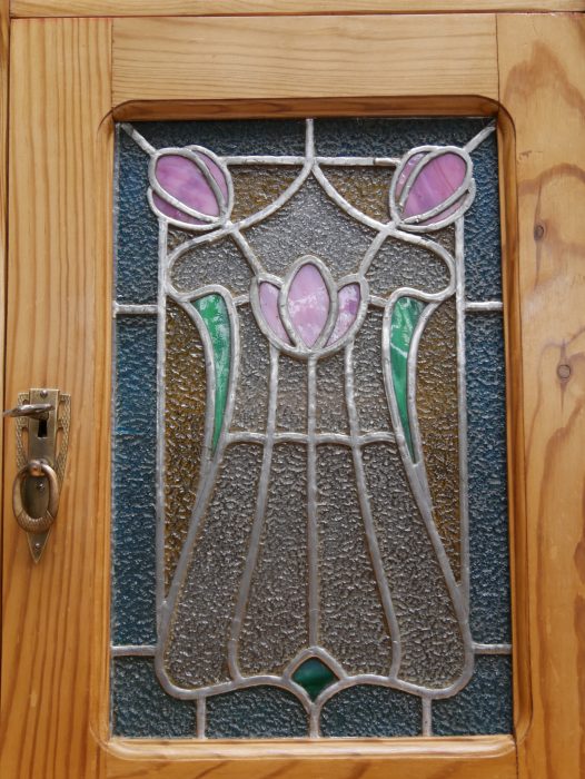 Nahaufnahme des originalen Bleiglasfensters mit floralem Jugendstilmotiv. Das historische Bleiglas besitzt lediglich leichte altersbedingte Gebrauchsspuren und gehört zur originalen Ausstattung.