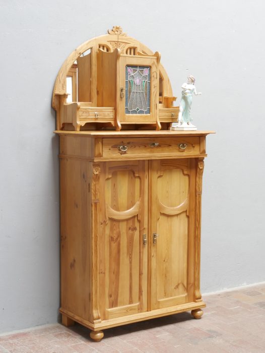 Außergewöhnlich aufwendig gestaltetes originales Jugendstil-Aufsatzvertiko aus Weichholz um 1900. Das restaurierte Möbel besitzt einen prachtvollen Aufsatz mit originalem Bleiglasfenster, zwei Spiegeln, kleinen Schubkästen sowie kunstvoll geschnitzten Jugendstil-Ornamenten und zählt zu den seltensten Ausführungen dieser Epoche.