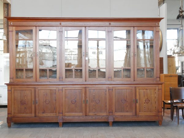 Hauptansicht einer außergewöhnlich großen originalen Jugendstil-Bibliothek um 1910 mit verglastem Oberteil und geschlossenem Unterschrank. Der zweiteilige Bibliotheks- und Ladenschrank befindet sich im unrestaurierten Originalzustand mit schöner Oberflächenpatina, Originalglas, Originalbeschlägen sowie höhenverstellbaren Einlegeböden mittels Zahnleisten.