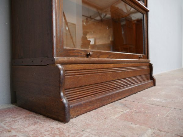 Detailaufnahme des unteren Sockelbereichs des originalen modularen Bookcase-Bücherschranks. Sichtbar sind die kräftige Sockelkonstruktion, die hochwertige Eichenholzoberfläche und die solide handwerkliche Ausführung des historischen Möbelstücks.
