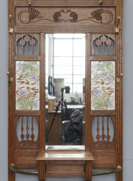 Detailansicht des oberen Bereichs der Garderobe mit Spiegel, geschnitzter Krone, seitlichen Ornamenten und originalen Jugendstil-Fliesen. Die Aufnahme zeigt die außergewöhnlich dekorative Gestaltung des Kopfteils.