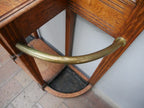 Detailansicht des geschwungenen Messingbügels zur Aufnahme von Regenschirmen im unteren Bereich der Garderobe. Die elegante Metallarbeit ergänzt die hochwertige Jugendstil-Ausführung des Möbelstücks.