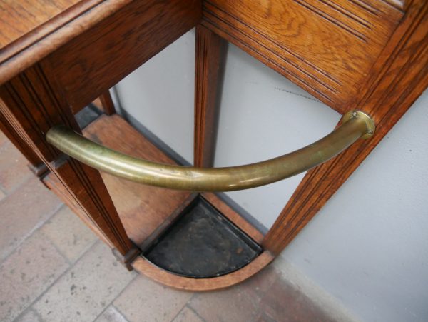 Detailansicht des geschwungenen Messingbügels zur Aufnahme von Regenschirmen im unteren Bereich der Garderobe. Die elegante Metallarbeit ergänzt die hochwertige Jugendstil-Ausführung des Möbelstücks.