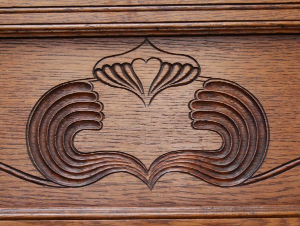 Detailaufnahme der geschnitzten Jugendstil-Ornamente im oberen Bereich der Garderobe. Die floralen Linien und die fein gearbeitete Holzstruktur spiegeln den typischen Jugendstil wider.