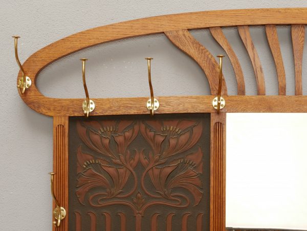 Detailaufnahme des oberen linken Garderobenbereiches mit den originalen Messinghaken, dem geschwungenen Aufsatz und der geprägten Lederfüllung. Die Aufnahme zeigt die hochwertige handwerkliche Ausführung bis ins kleinste Detail.

