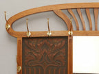 Detailaufnahme des oberen linken Garderobenbereiches mit den originalen Messinghaken, dem geschwungenen Aufsatz und der geprägten Lederfüllung. Die Aufnahme zeigt die hochwertige handwerkliche Ausführung bis ins kleinste Detail.
