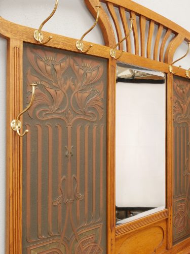 Detailansicht einer geprägten Lederfüllung neben dem Facettenspiegel. Die Aufnahme zeigt die fein gearbeitete Lederprägung, die Messinghaken und die harmonische Verbindung von Holz, Leder und Spiegelglas.

