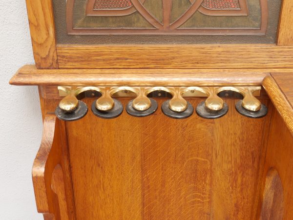 Detailaufnahme der dekorativen Zahnleiste unterhalb der Ablage. Die fein geschnitzten Holzelemente unterstreichen den hohen handwerklichen Anspruch und ergänzen die aufwendig gestalteten Lederfüllungen der Jugendstil-Garderobe.

