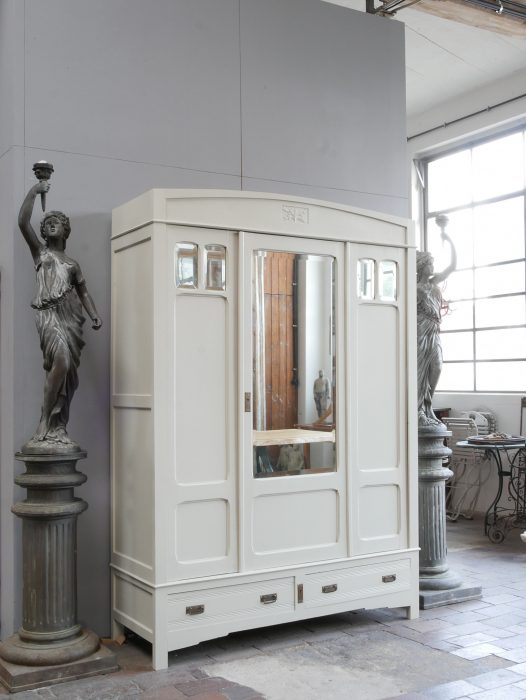 Eleganter restaurierter Jugendstil-Kleiderschrank aus Frankreich um 1900 in hellem Farbton „Old White“. Dreitüriger Schrank mit originalem Facettenspiegel, kleinen Spiegeln in den Seitentüren, dekorativen Jugendstil-Ornamenten sowie zwei großen Schubladen im Sockel. Gesamtansicht des außergewöhnlichen Originalmöbels.
