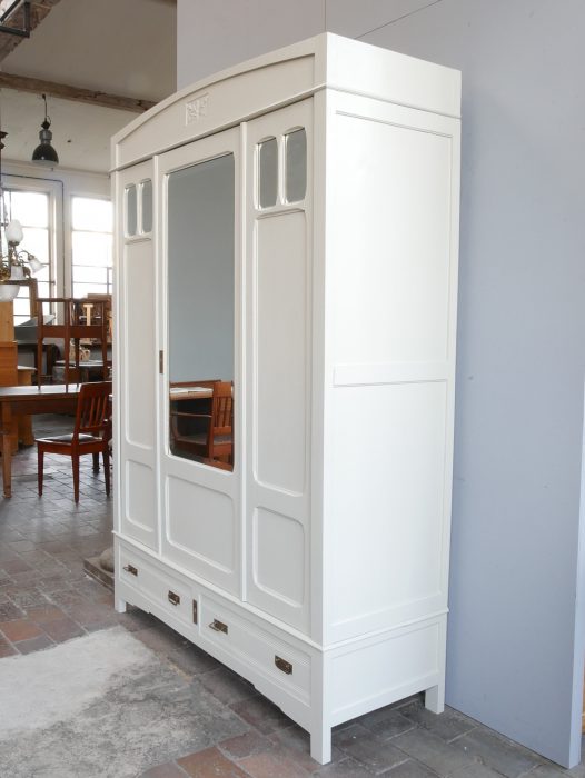 Seitenansicht des restaurierten Jugendstil-Kleiderschranks aus Frankreich. Gut erkennbar sind die aufwendig gestalteten Seitenfüllungen, die harmonischen Proportionen sowie die elegante helle Farbgestaltung des originalen Möbelstücks.
