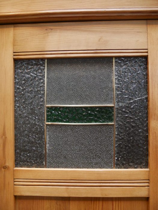 Detailaufnahme eines originalen Bleiglasfensters mit strukturierter Verglasung und dekorativer Bleisprosse. Das historische Glas verleiht dem Kleiderschrank seinen unverwechselbaren Jugendstil-Charakter.