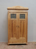 Frontansicht des restaurierten Jugendstil-Kleiderschranks mit originalen Bleiglasfenstern, geschnitzten Türfüllungen und dekorativem Giebelaufsatz. Die harmonischen Proportionen und die gewachste Weichholzoberfläche unterstreichen den eleganten Charakter des historischen Schranks.
