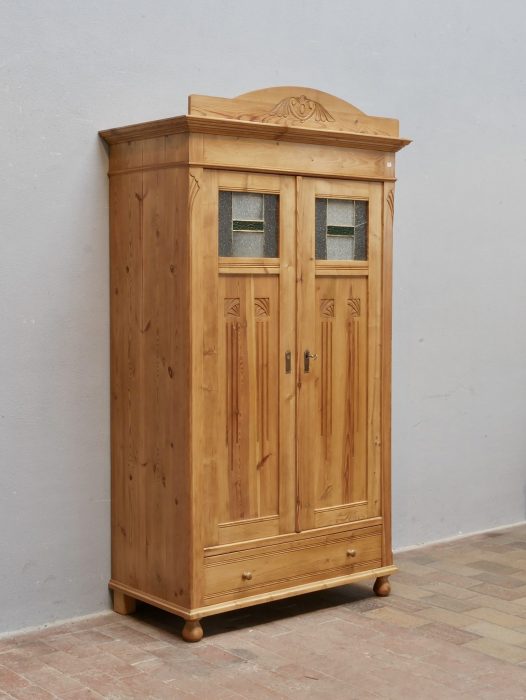 Wunderschöner originaler Jugendstil-Kleiderschrank aus Weichholz um 1900 in wohnfertig restauriertem Zustand. Der zweitürige Schrank besitzt originale Bleiglasfenster, aufwendig geschnitzte Jugendstil-Ornamente an Türen und Seiten, einen originalen abnehmbaren Aufsatz sowie einen Schubkasten im Sockelbereich.
