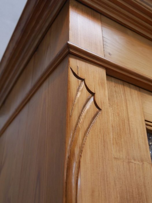 Detailaufnahme der geschnitzten Jugendstil-Verzierungen an der Seitenwand des Kleiderschranks. Die fein ausgearbeiteten Ornamente unterstreichen die hohe handwerkliche Qualität des historischen Möbels.